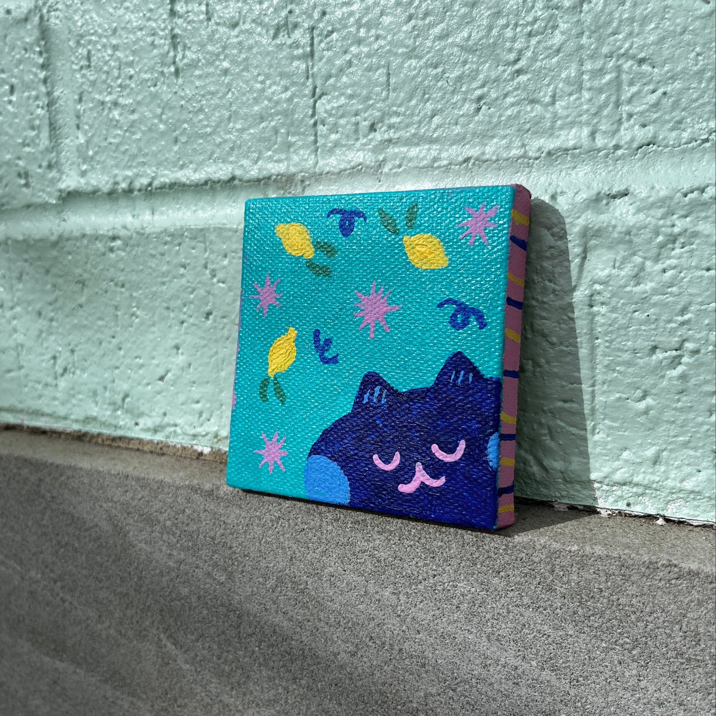 Colorful rectangular canvas with a cat painting design perched on a textured wall.