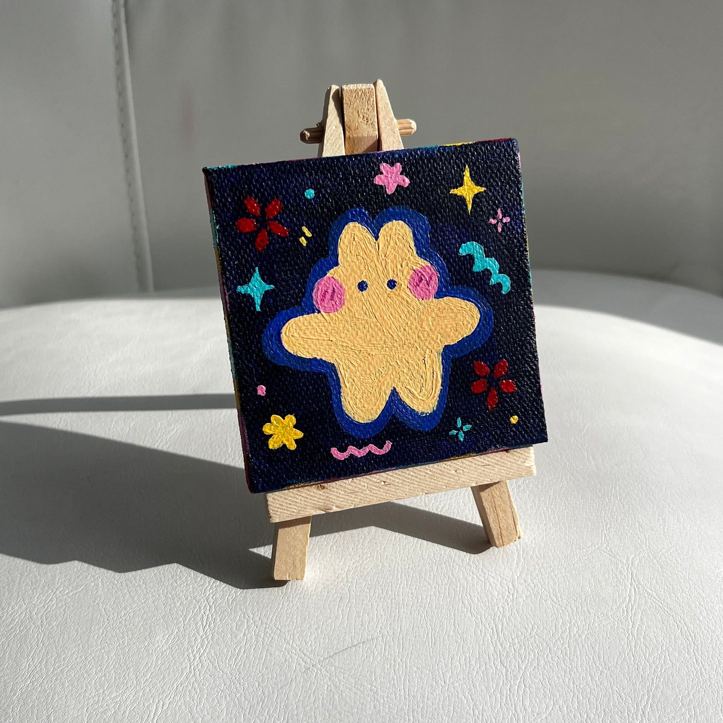 Square painting of a cream bunny on a miniature easel against a neutral background