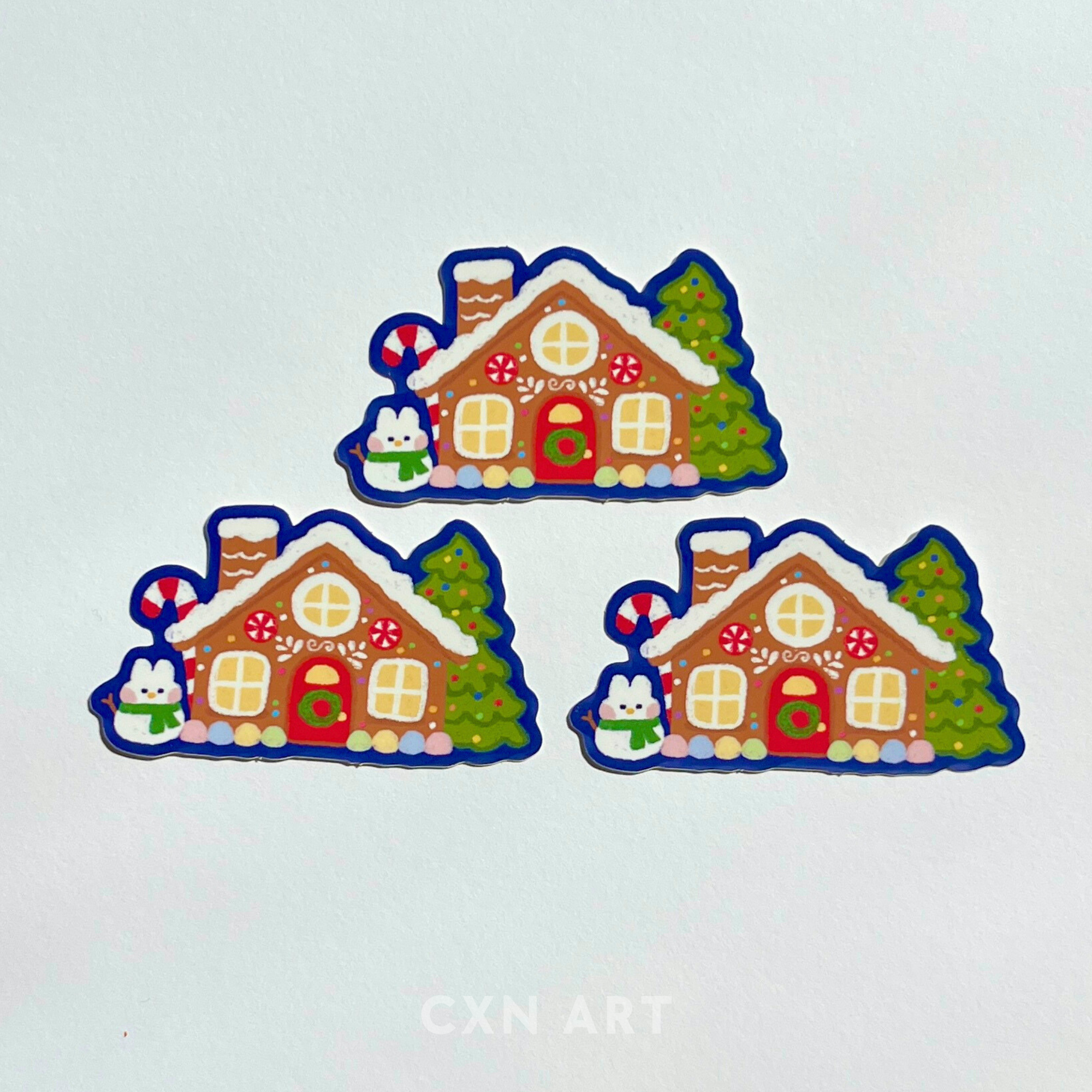 Set of three colorful illustrated gingerbread house-shaped stickers on a light gray-white background.