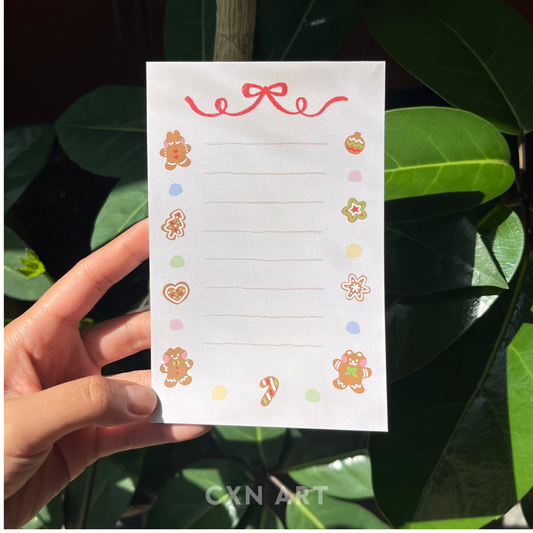 Hand holding a note pad memo pad with decorative gingerbread illustrations against a leafy background