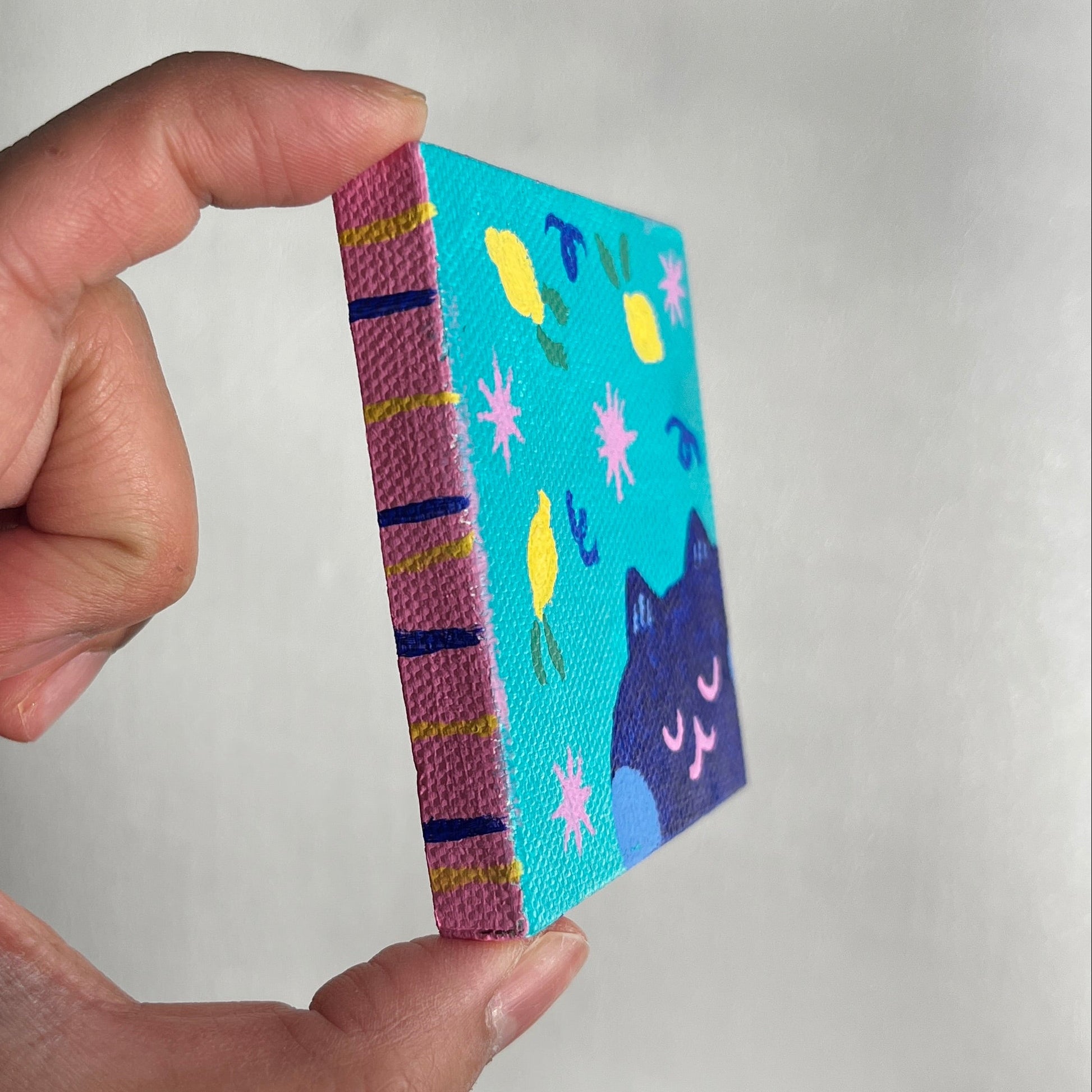 Hand holding a colorful small canvas with pinnk, blue, yellow fore-edge 