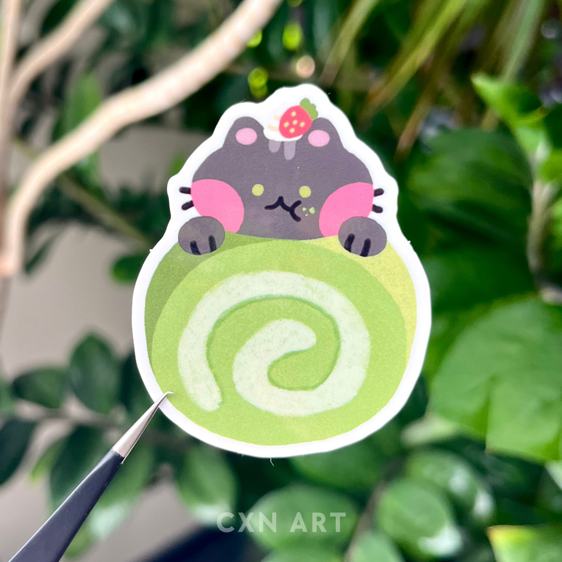 Sticker of a black cat with green eyes holding onto a green matcha green tea strawberry roll with a strawberry on the cat's head against a leafy background