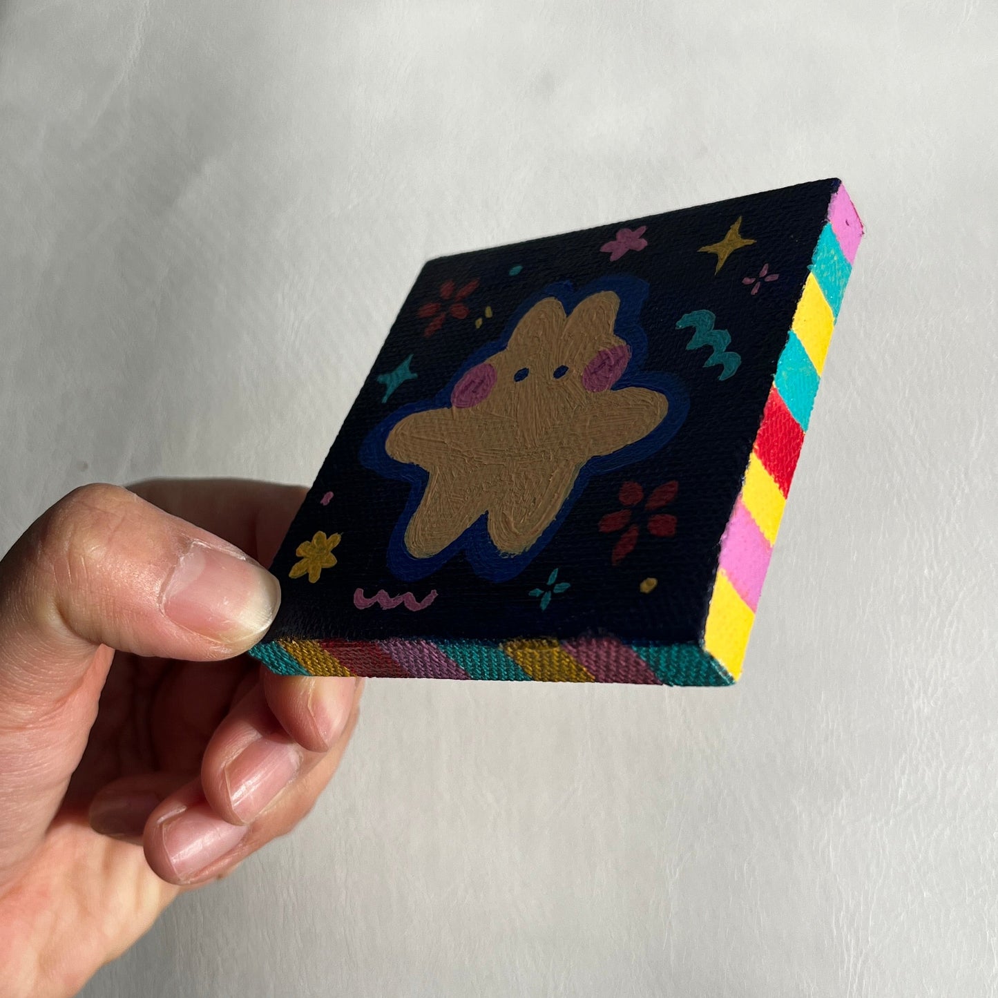 Hand holding a small, colorful painting with a cream bunny against a plain background